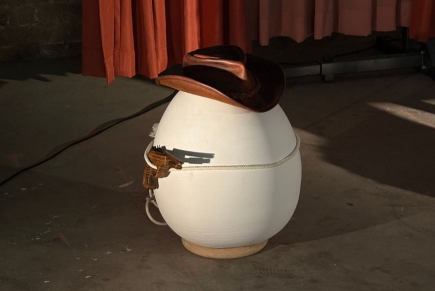 An egg-shaped figuring with a brown cowboy hat and a pistol. 