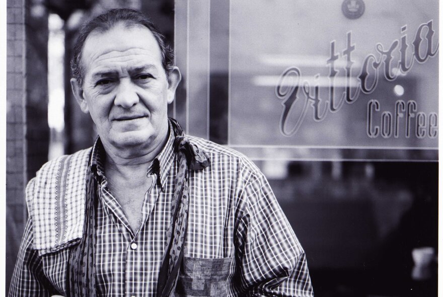 Pellilgrinis founder Sisto Malaspina standing with teatowel on his shoulder in front of a Vittoria coffee sign.