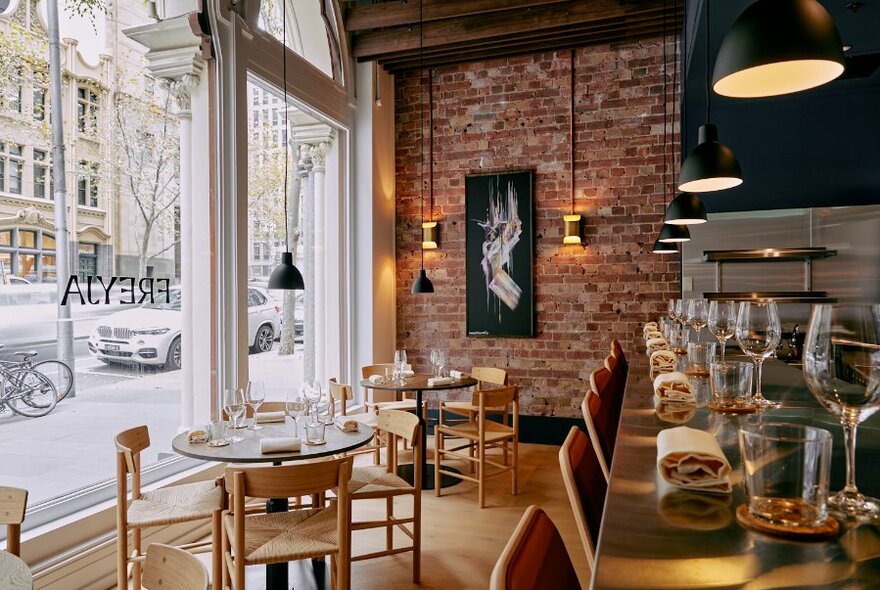 Restaurant interior looking onto Collins Street with wooden tables set for dining.