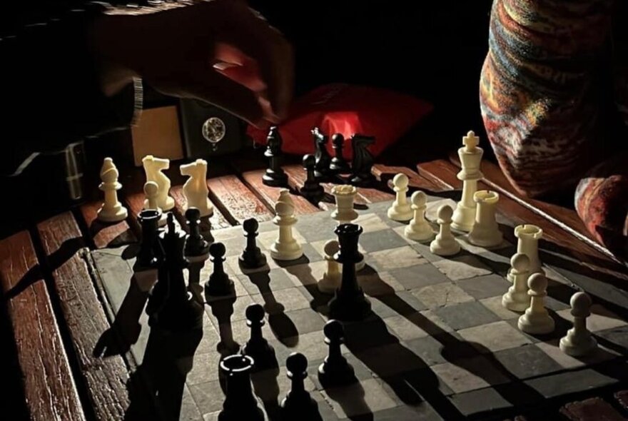 A chess board set up with pieces, the light behind causing shadows to fall on the board.