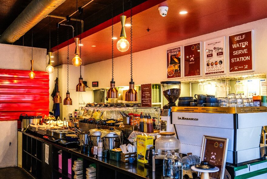 Cosy, warmly lit Korean restaurant with American diner-style interior design: hanging lights, red paint accents, white coffee machine; and a self-serve buffet station.