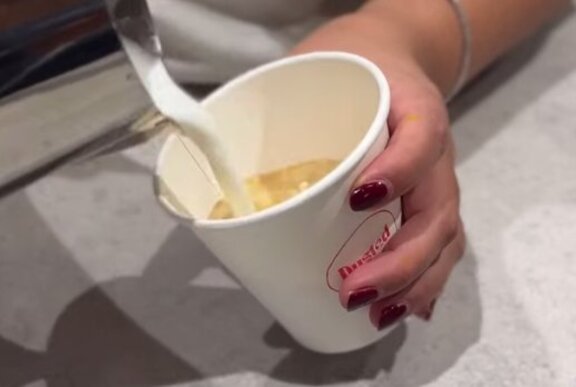 Hands pouring milk into a takeaway cup of coffee.
