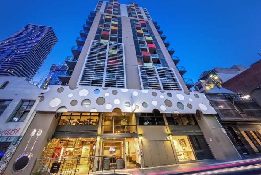 A high-rise building at dusk, the bottom two stories lit for the evening with yellow lighting.