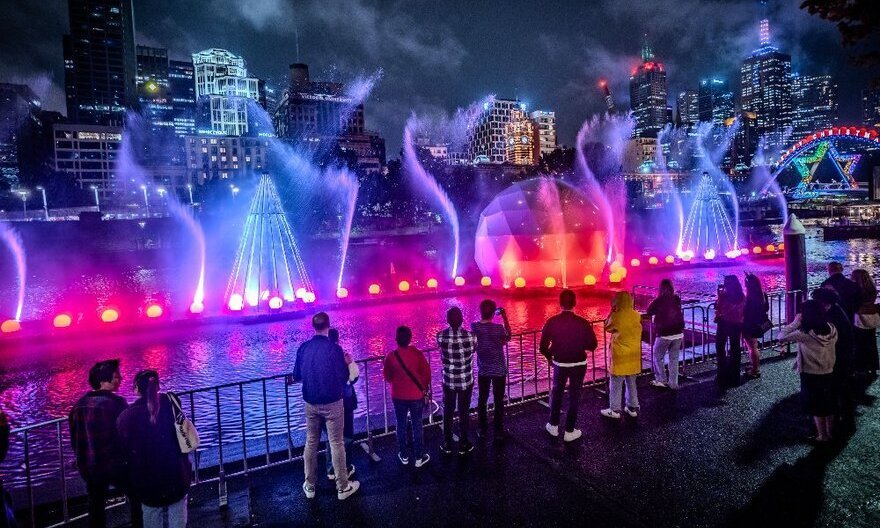 Rainbow lights on water jets and a giant bauble on the river at night.