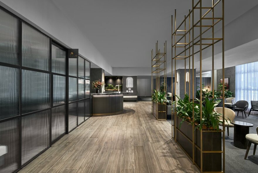 The large and spacious lobby of the Melbourne Marriott Hotel, showing reception desk at the end of the space, club chairs and coffee tables in a lounge area behind a partition filled with green plants. 