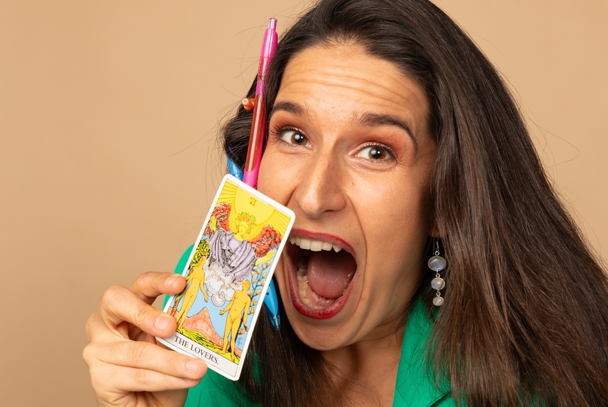 A woman with her mouth open wide looking surprised, holding a tarot card near their face.