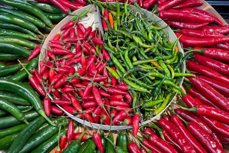 A bowl of small chillis, divided in half with red chillis on one side and green on the other, surrounded by larger chillis of the opposite colour.