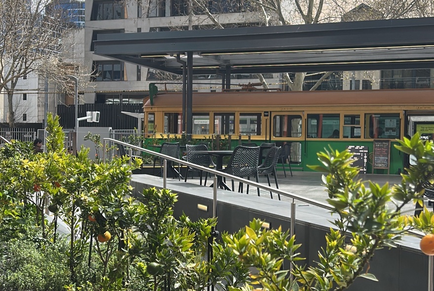 A garden setting with an old Melbourne Tram parked under a canopy with tables and chairs. 