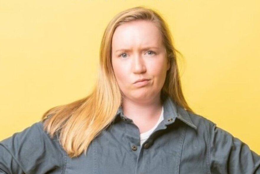 Woman with side-parted long blonde hair, wearing a grey shirt with a quizzical expression.