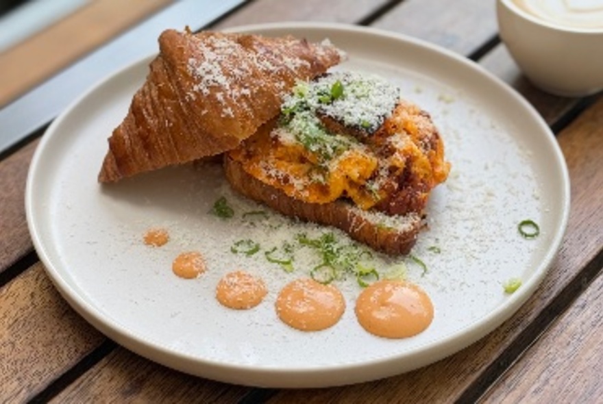 A plate with a Gochujang scrambled egg croissant, with five dollops of sauce in different sizes. 