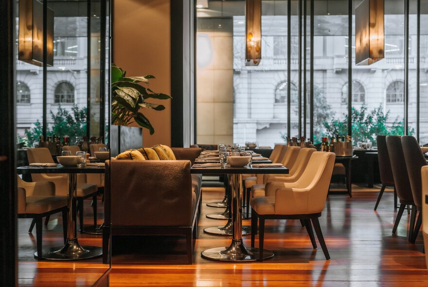 An up-market dining space in a hotel, with long pendulum lights hanging from the ceiling and a window reflecting a heritage building across the road. 