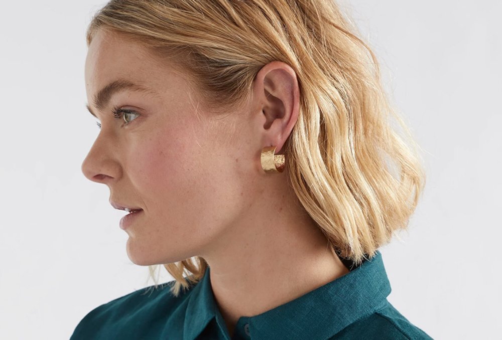 A close up of a blonde woman wearing a gold hoop earring.