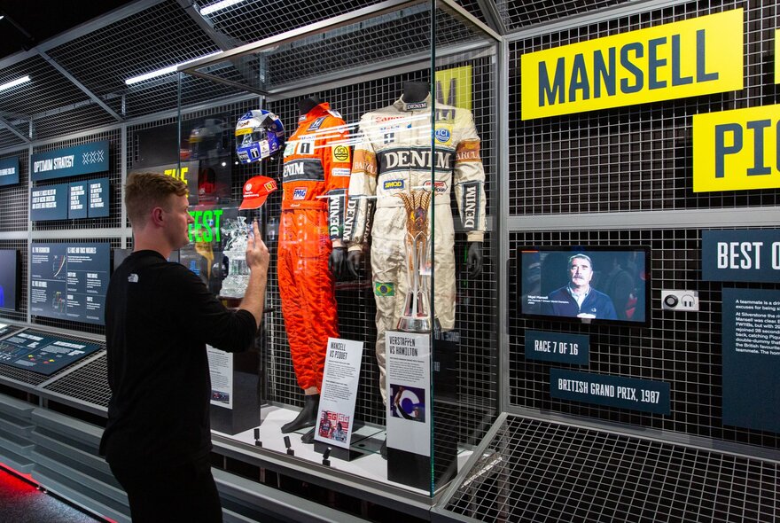 A man looks at a cabinet with F1 driver uniforms and other memorabilia.