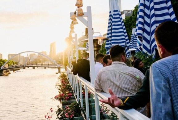 Patrons hanging out against a white fence, overlooking the Yarra River as the sun is setting.