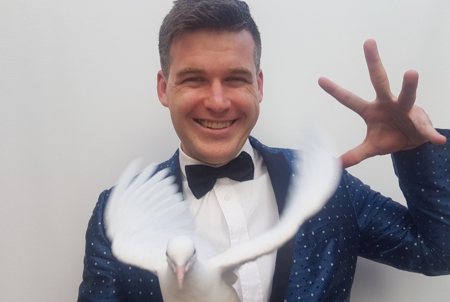 Magician Ashley appearing on stage with one of his white doves.