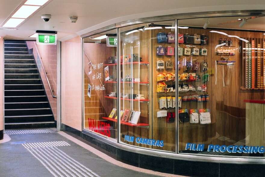 The rounded shop window at Walkens House of Film in Campbell Arcade basement, with stairs to the left leading to street level.