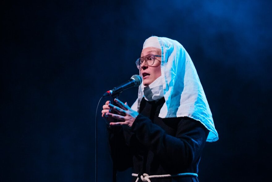 Close-up of comedian Scout Boxall on stage wearing a nun's habit and talking into a microphone.