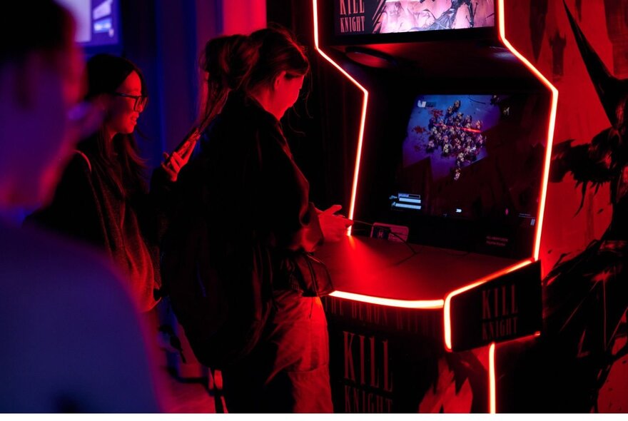 People playing arcade games outlined in lights in dark setting.