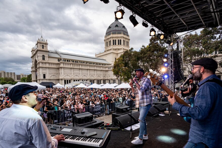 A live band on stage, with a large crowd in front of the Royal Exhibition Building in Melbourne.
