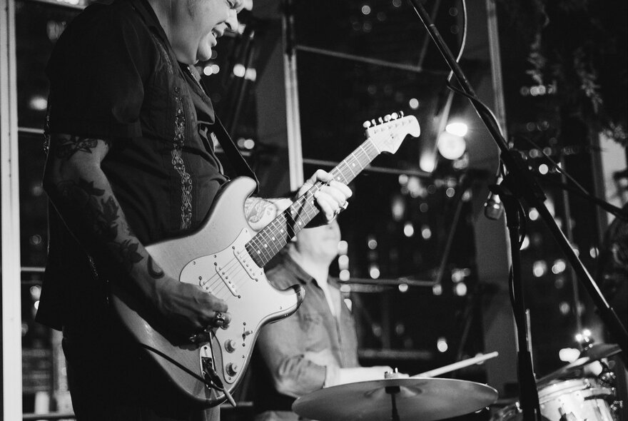 Live band playing in a venue with windows.