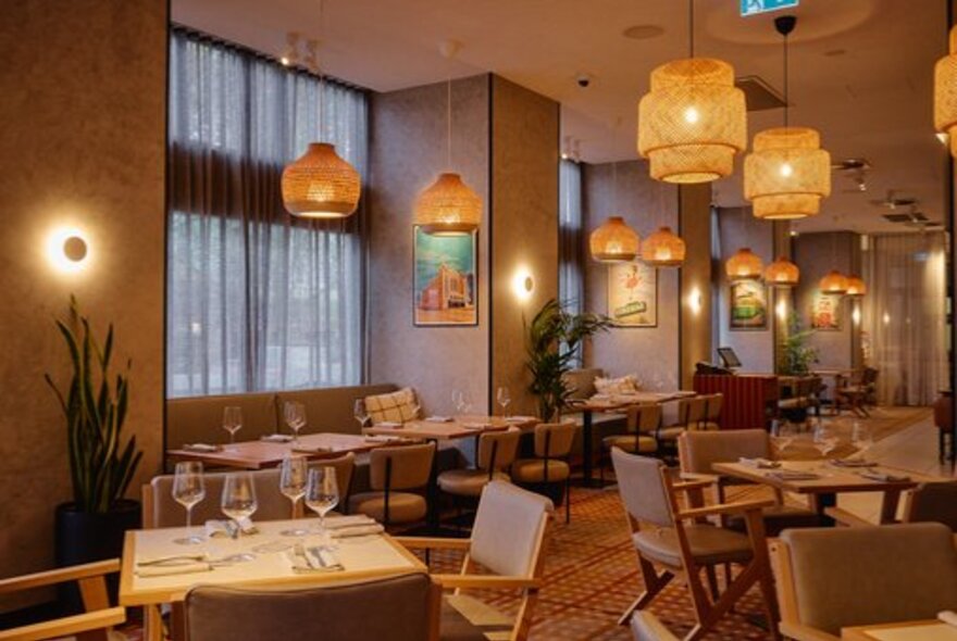 Interior of One Queen restaurant with warm hanging lights, tables and chairs in neutral colours, green plants and artwork on the walls.