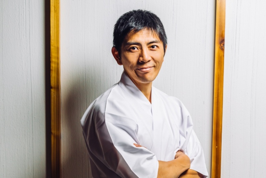 Chef Norihito Endo, standing with arms crossed, wearing white Japanese-style chefs whites.