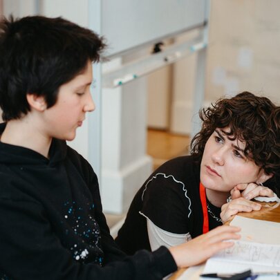 A teachers bobs down next to a seated student and listens intently. 