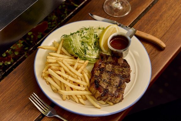 Plate of steak with shoestring fries, a wedge of iceberg lettuce salad and a jug of sauce on side.