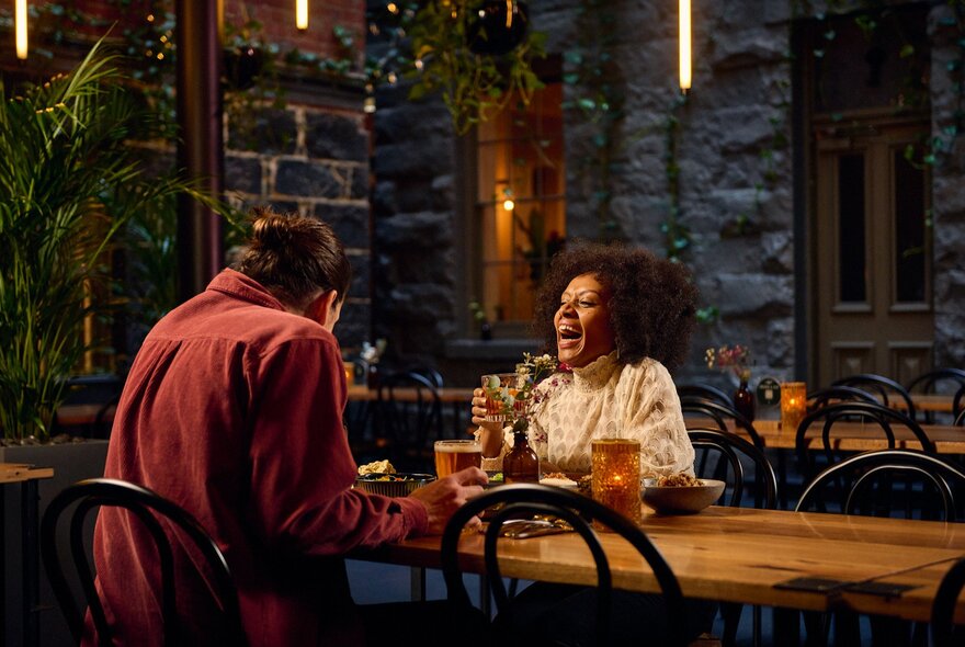 A couple laughing with drinks in a pub with bluestone walls.