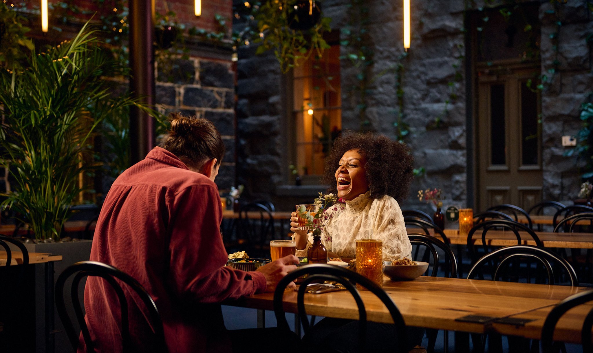 A couple laughing with drinks in a pub with bluestone walls.