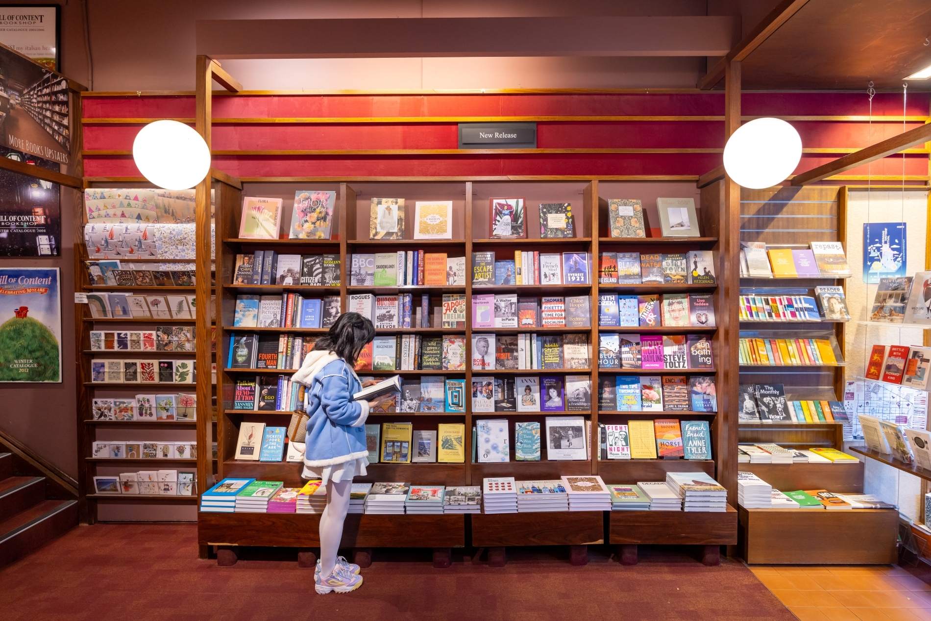 A customer reads a book in a bookshop in front of a large bookcase