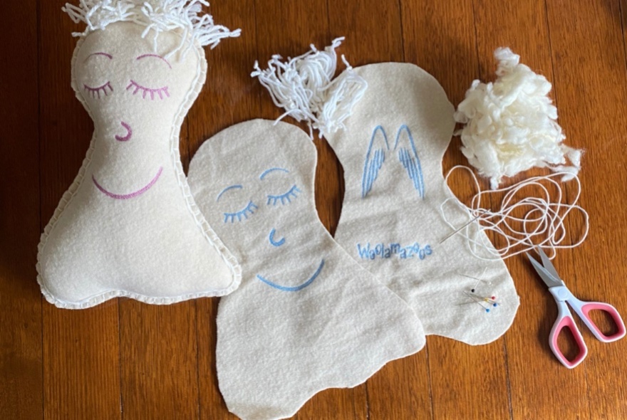 Cut out pieces of white wool, with thread, scissors and stuffing, ready to be sewn into plush soft angels.