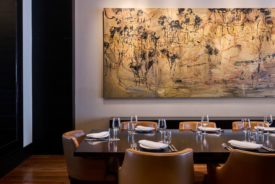 Private dining table set for dining in a rooom with a large beige artwork on the wall.