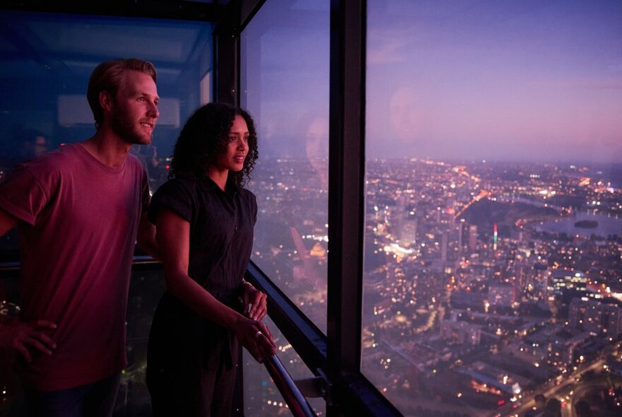 A couple looking over the Melbourne city scape from the 88th floor of The Edge, a glass cube at the Eureka Tower.