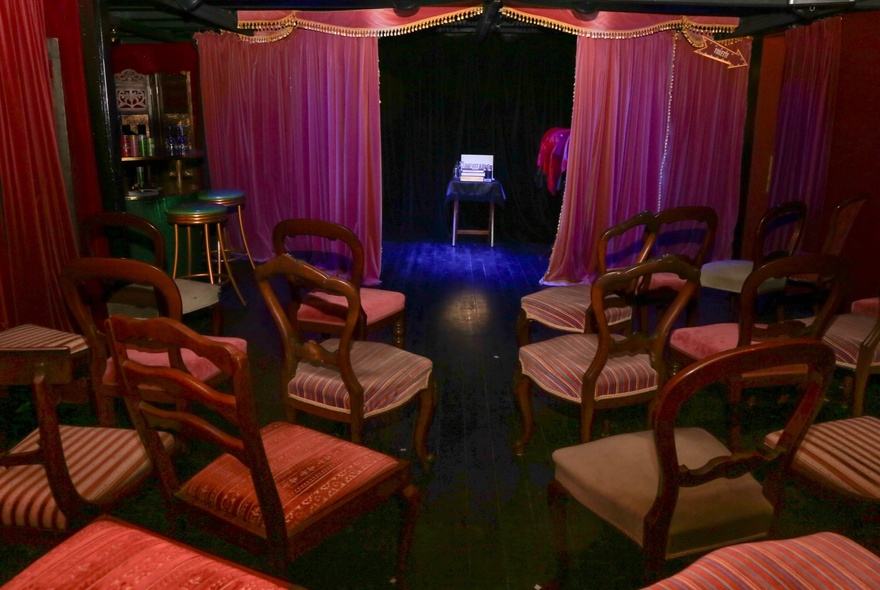 Small venue with curtained stage and vintage dining chairs.