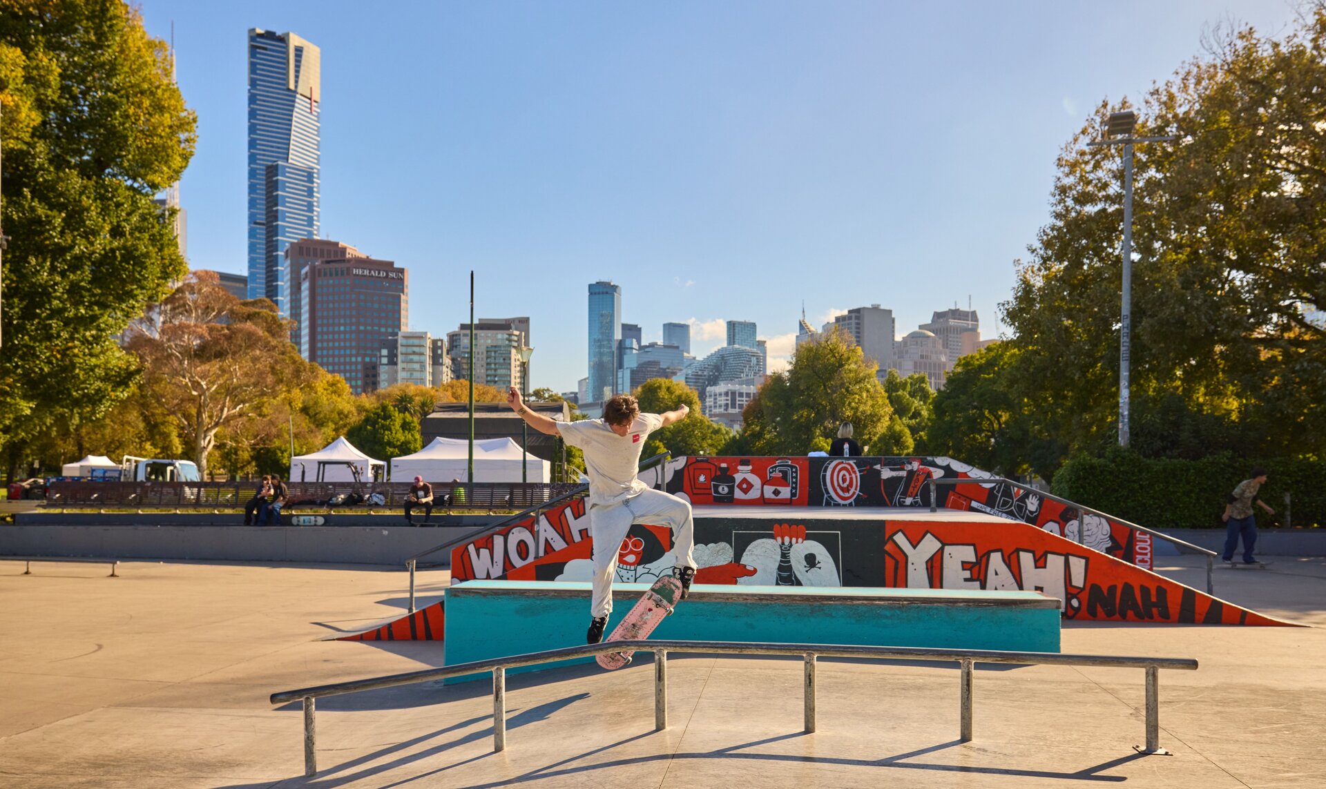 A man doing a skateboard trick in a Melbourne skate park on a sunny day.