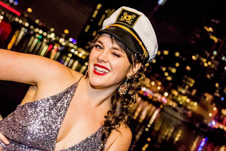 Woman in sequinned dress wearing a sailor's cap, winking.