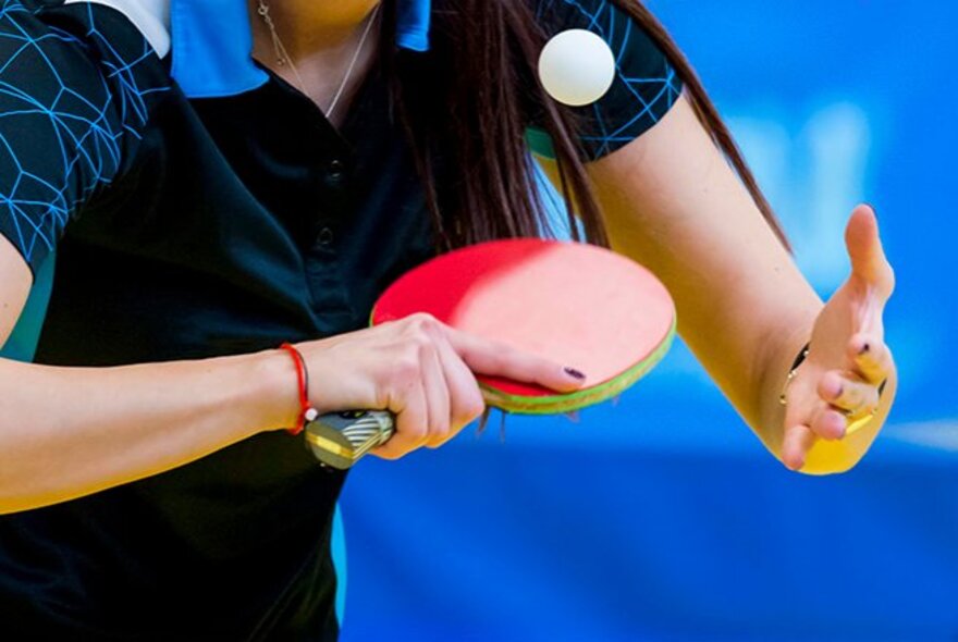 A person playing table tennis holding a red bat, about to hit the white table tennis ball.