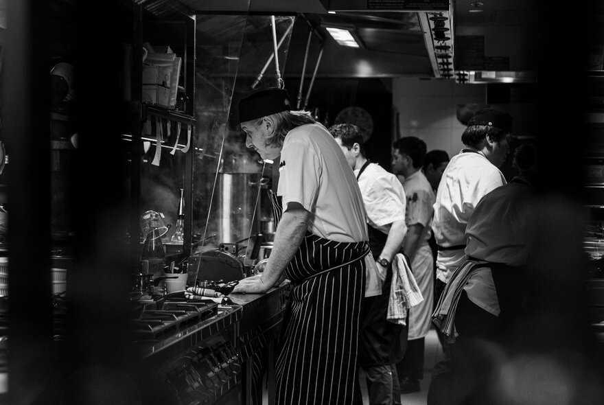 A black and white photograph of chefs in a restaurant kitchen.