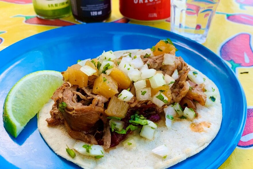 Blue plate holding an open tortilla with meat and potatoes with a slice of lime.