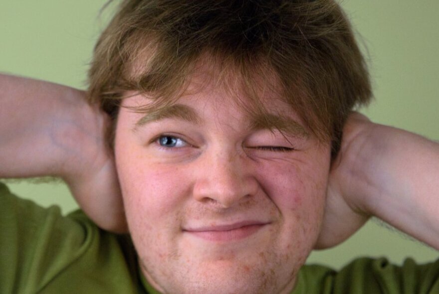 Close up of a man with one eye closed and both hands over his ears.