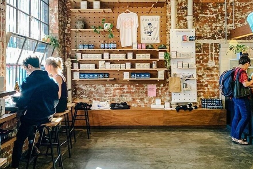 Interior of Seven Seeds with people dining at window bench seat, and a wall display of products for sale.