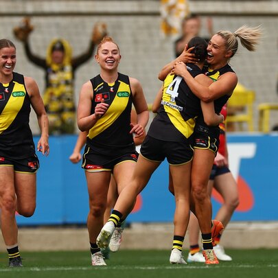 Four Richmond Tigers AFLW players celebrating a goal during a game.