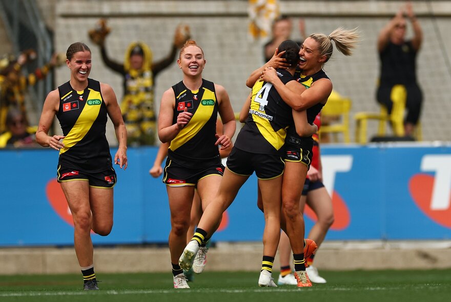 Four Richmond Tigers AFLW players celebrating a goal during a game.