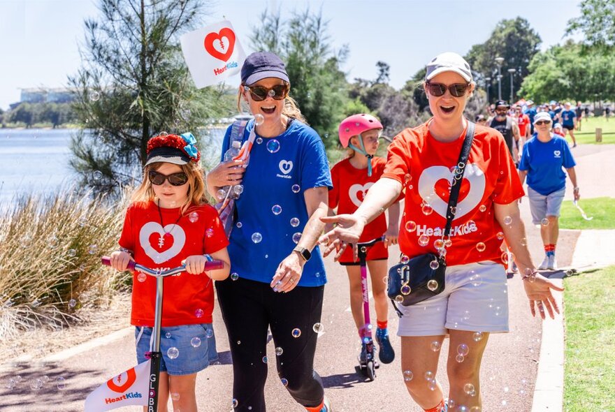 Adults and children participating in a charity walk around a body of water on a bright sunny day.