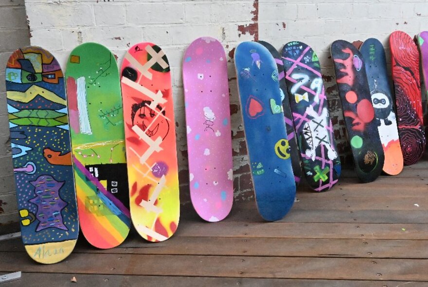 Colourfully painted skateboard decks lined up in a row on floorboards.