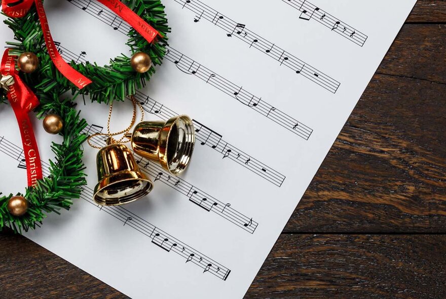 A song sheet resting on a dark wooden surface, with christmas bells on top.