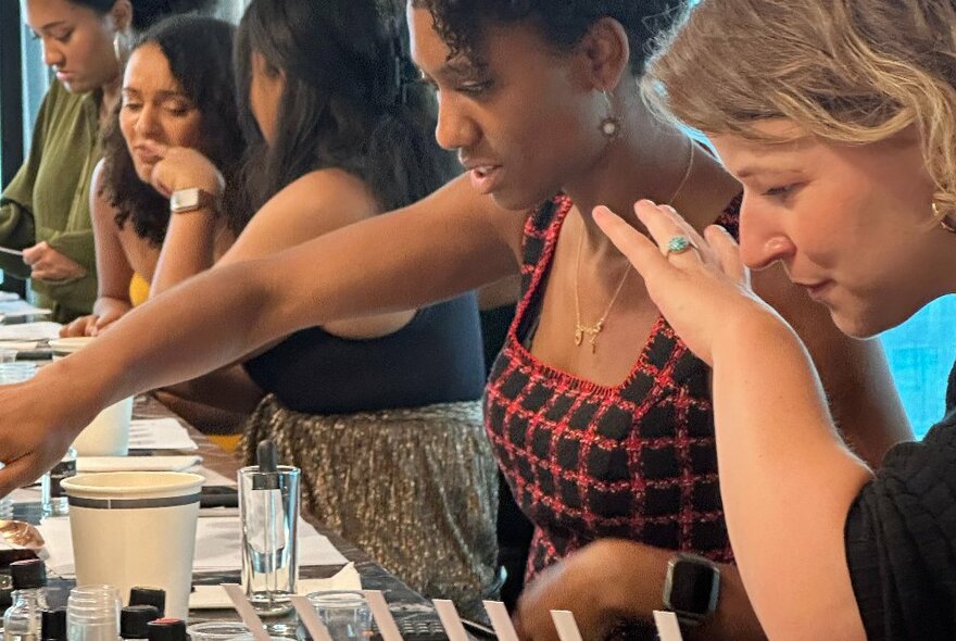 A row of people at a perfume workshop, all actively smelling or mixing. 