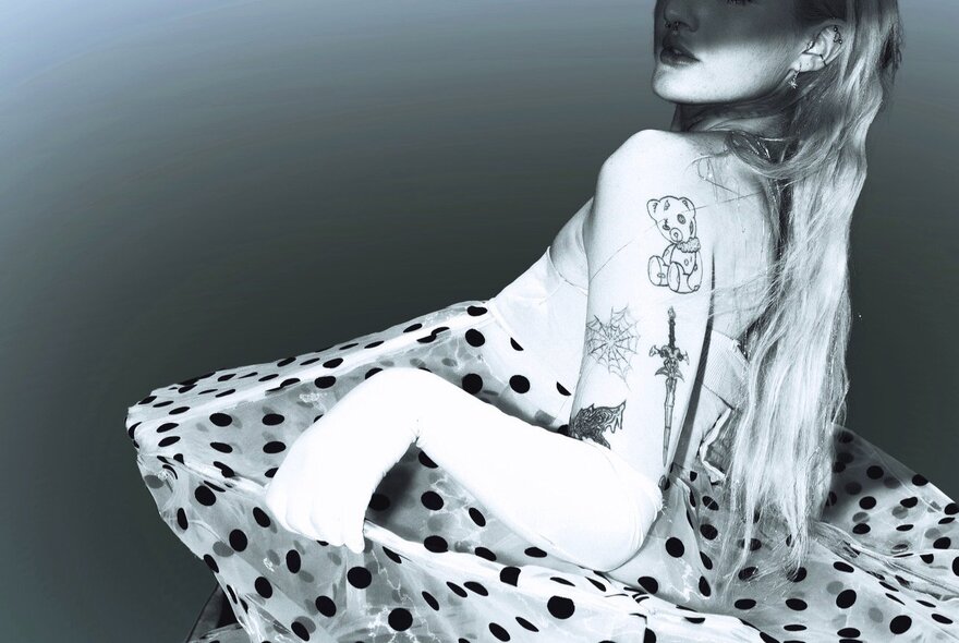 Models tattooed arm holding a polkadot gown, with long blonde hair.