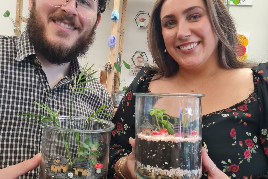 Two people holding glass-domed terrariums, smiling.